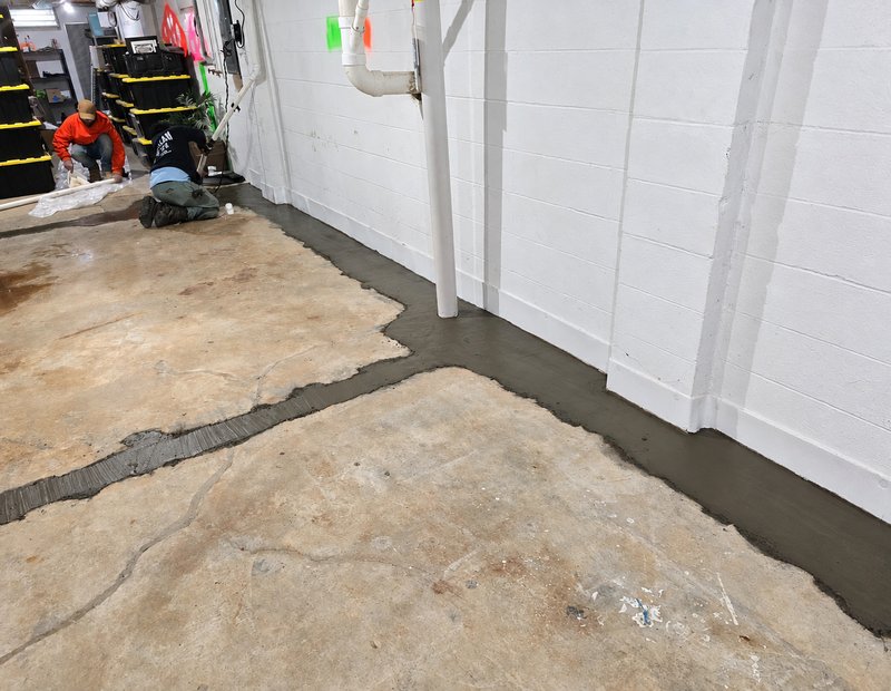 Technicians installing an interior basement waterproofing system